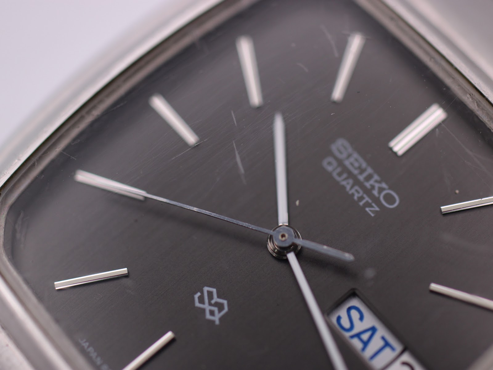 Close-up of the Seiko black dial, showing the quartz branding, SQ logo, and scratches on the crystal.