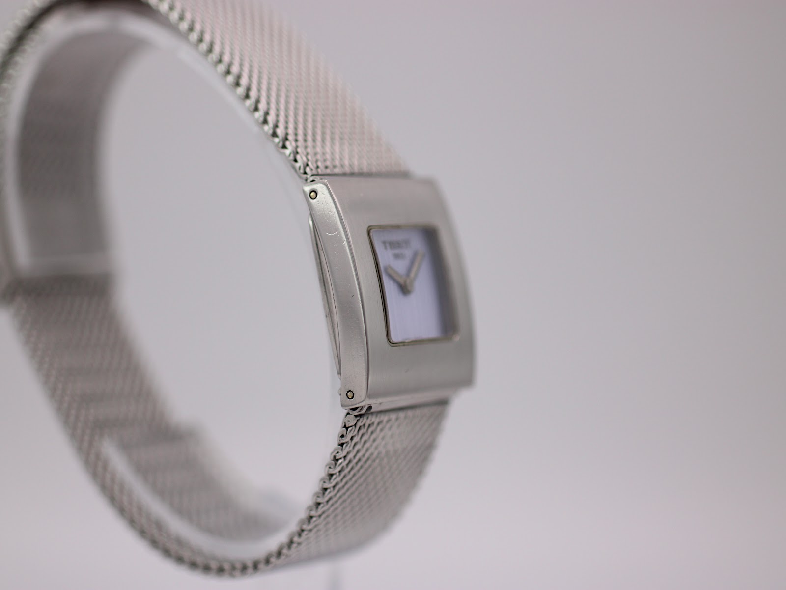 Angled side view of the Tissot L610K case and mesh bracelet on a display stand.
