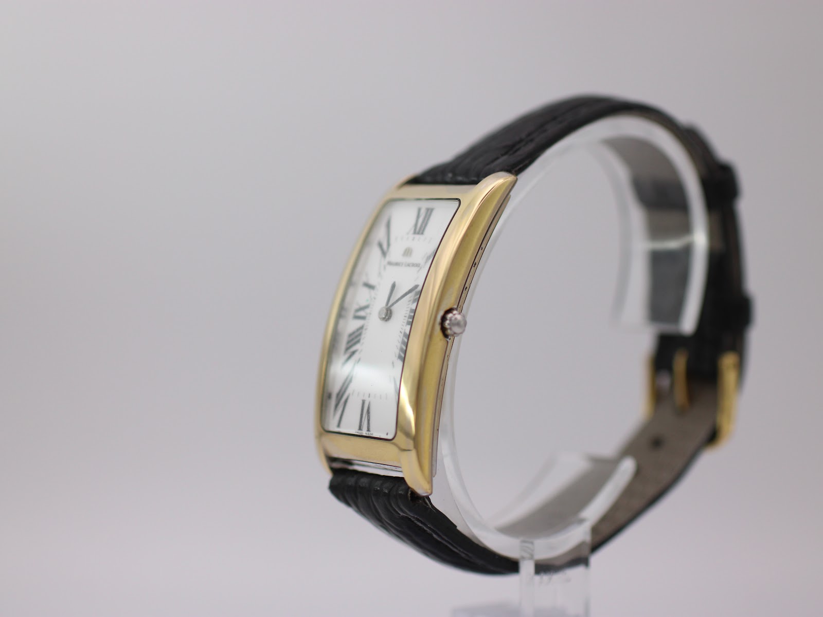 Angled side view of the Maurice Lacroix watch, showing the curved gold-plated case and crown, with the black leather strap.