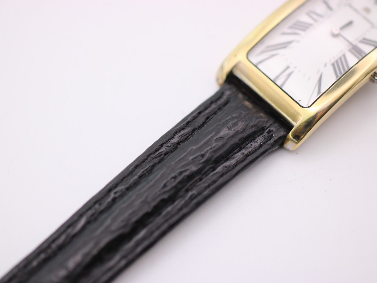 Detail shot of the black textured leather strap and lug area of the gold-plated watch case.
