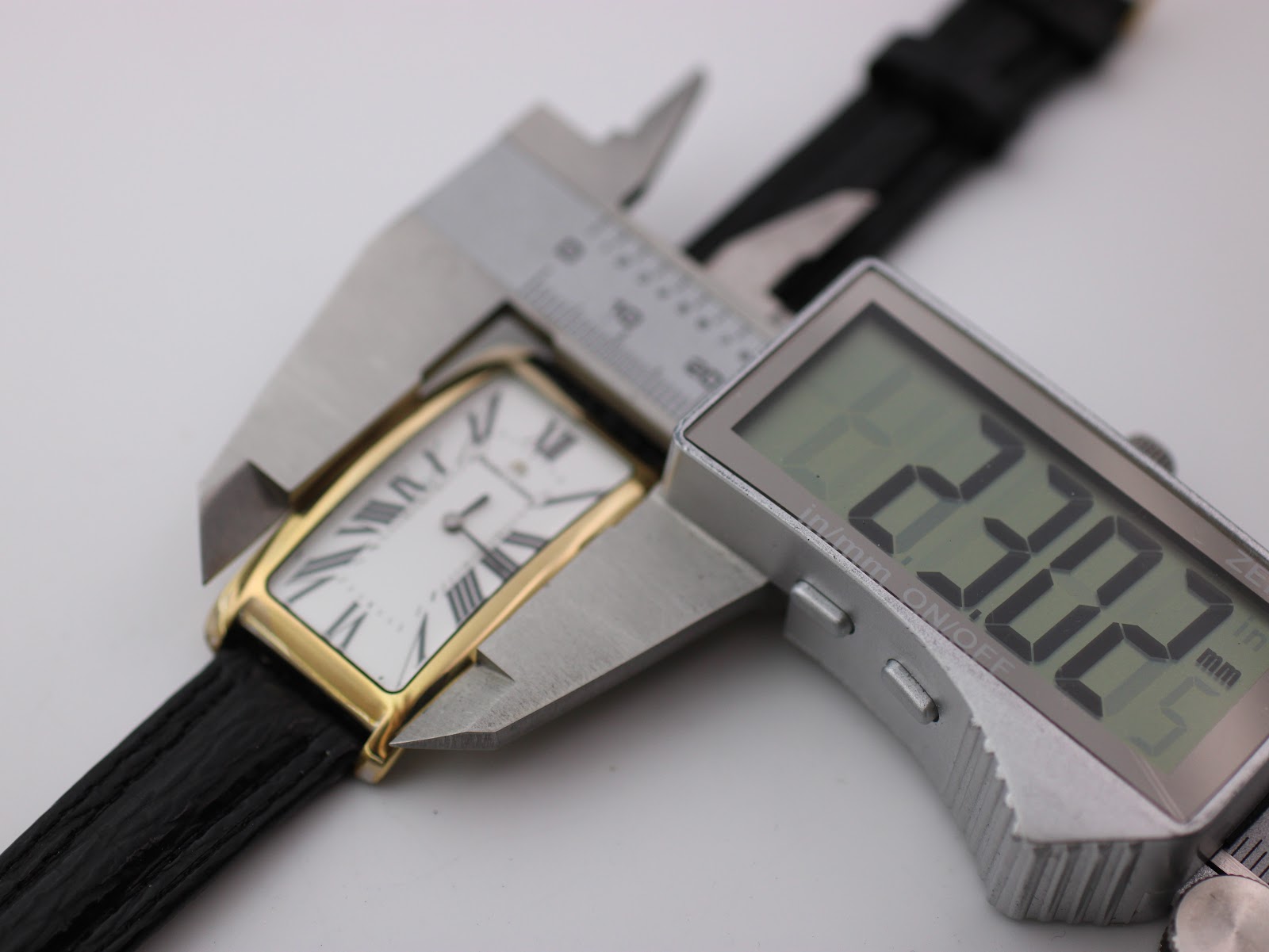 Digital caliper measuring the watch case width at 23.30mm, showing the white dial.