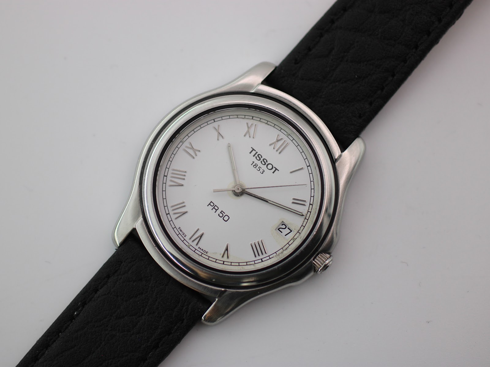 Overhead view of Tissot PR 50 watch with black leather strap on a white surface.