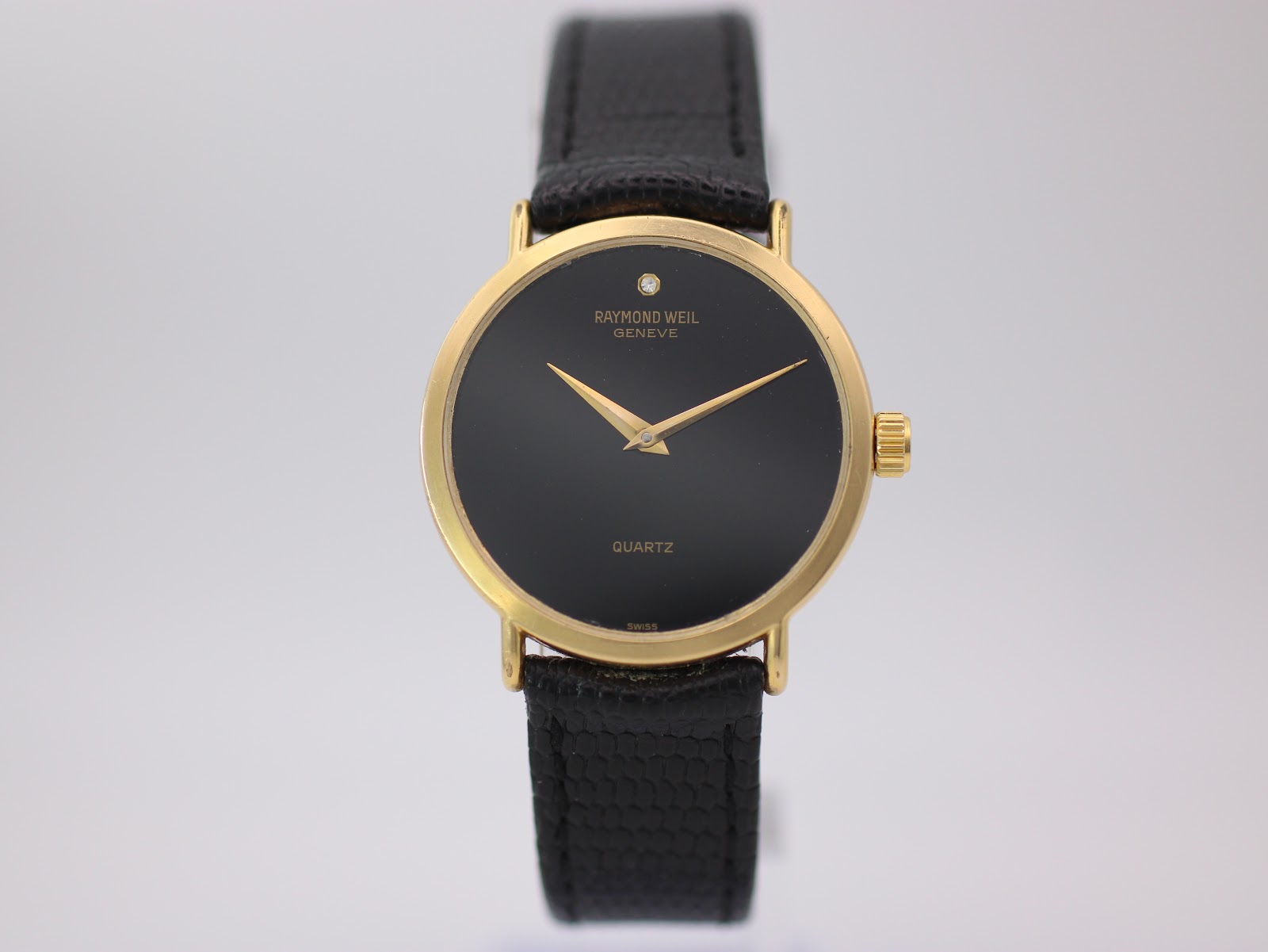 Close-up front view of Raymond Weil 5508 watch with black dial, gold hands, and diamond marker, on a black lizard grain strap.