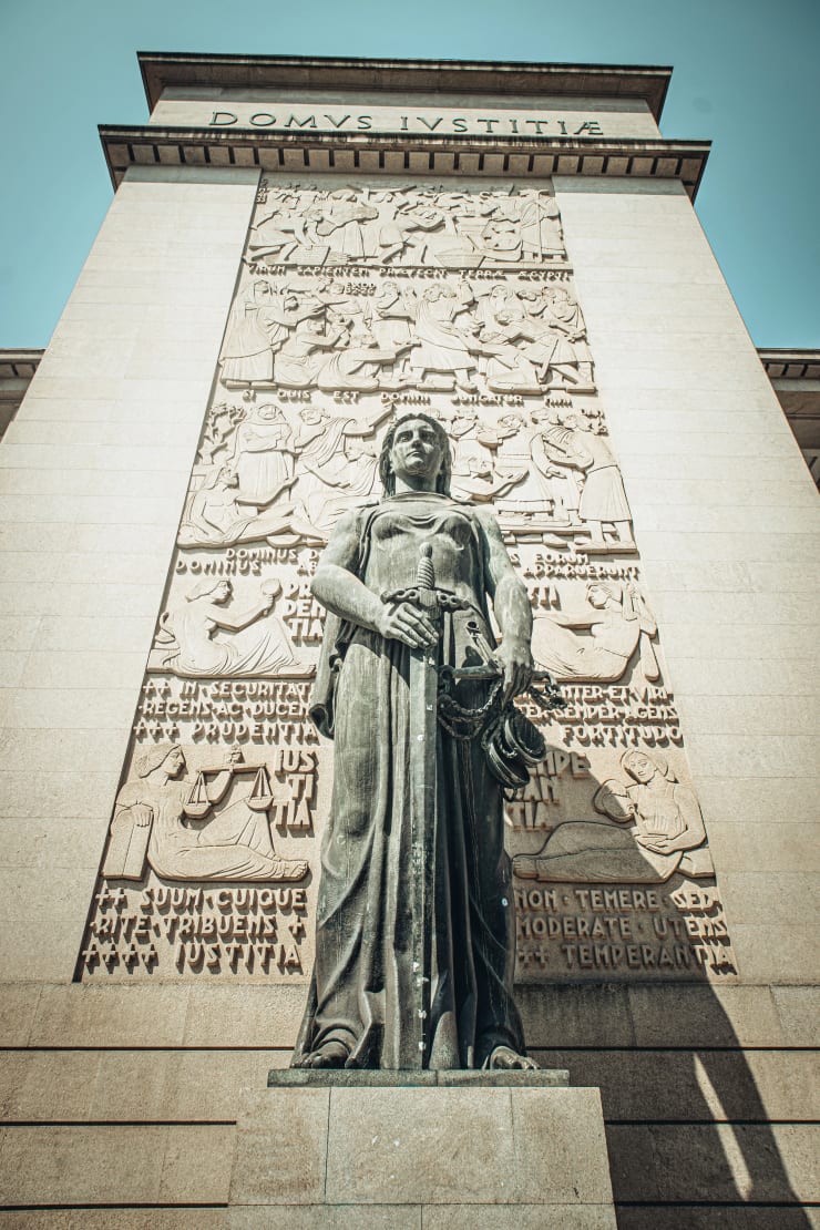 Statue de la Justice tenant une balance devant un palais de justice