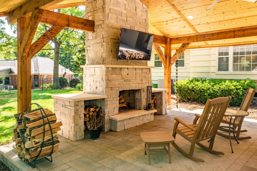 A covered patio with a stone fireplace and mounted television in Prairie Village, Kansas
