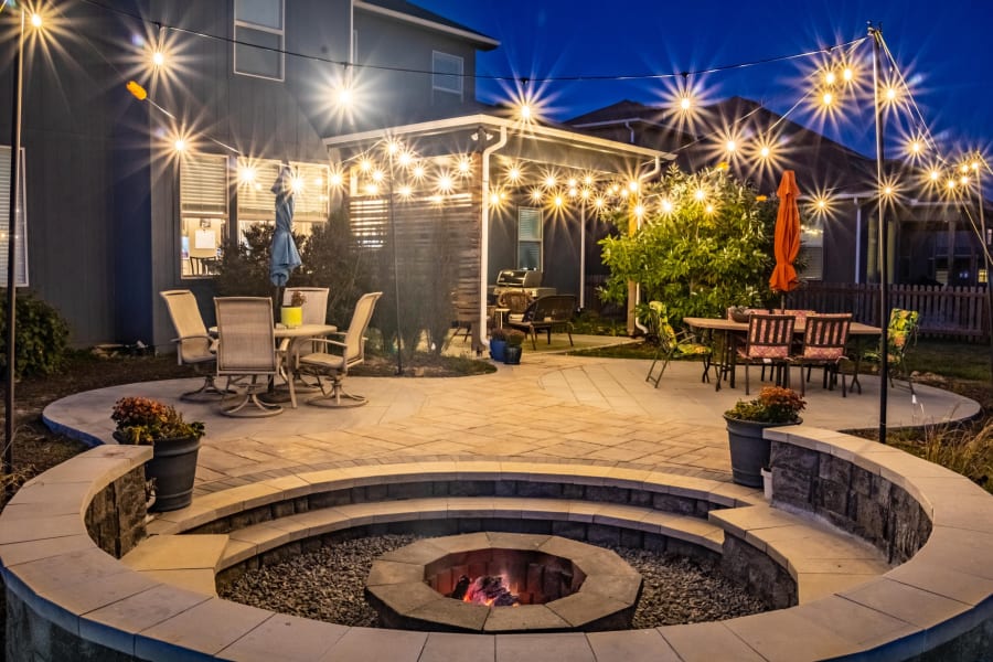 String lights over a paver patio and a lit sunken fire pit at night in Kansas City