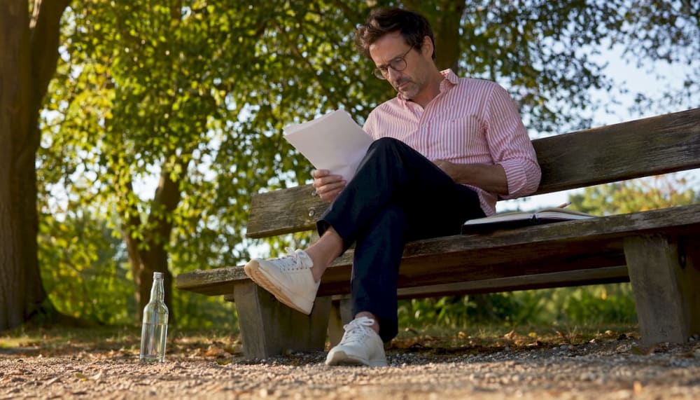 Homme lisant des documents assis sur un banc dans un parc