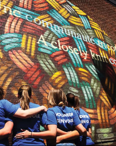 four people with backs facing camera wearing volunteer shirts in front of graffiti wall