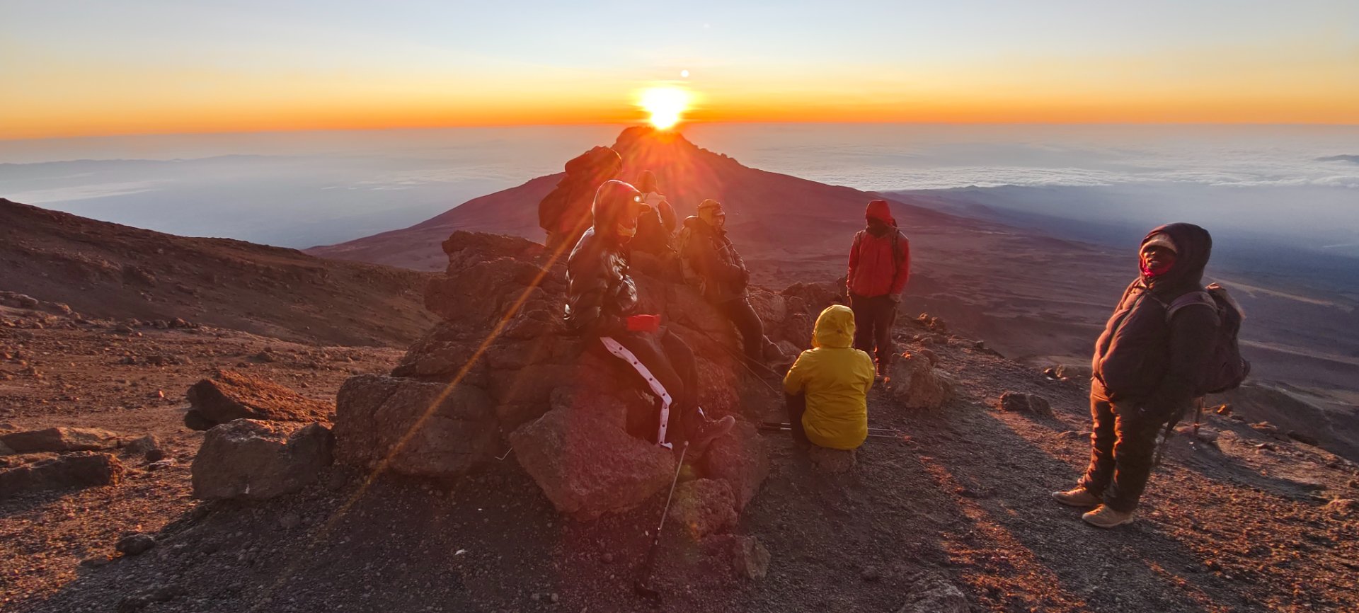 Successful climbers celebrating at Uhuru Peak with glaciers and summit sign