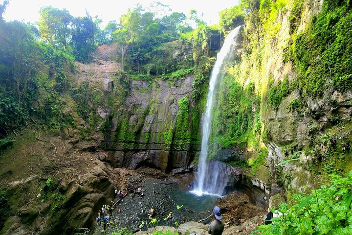 Travelers standing near lush tropical waterfalls on the slopes of Mount Meru near Arusha