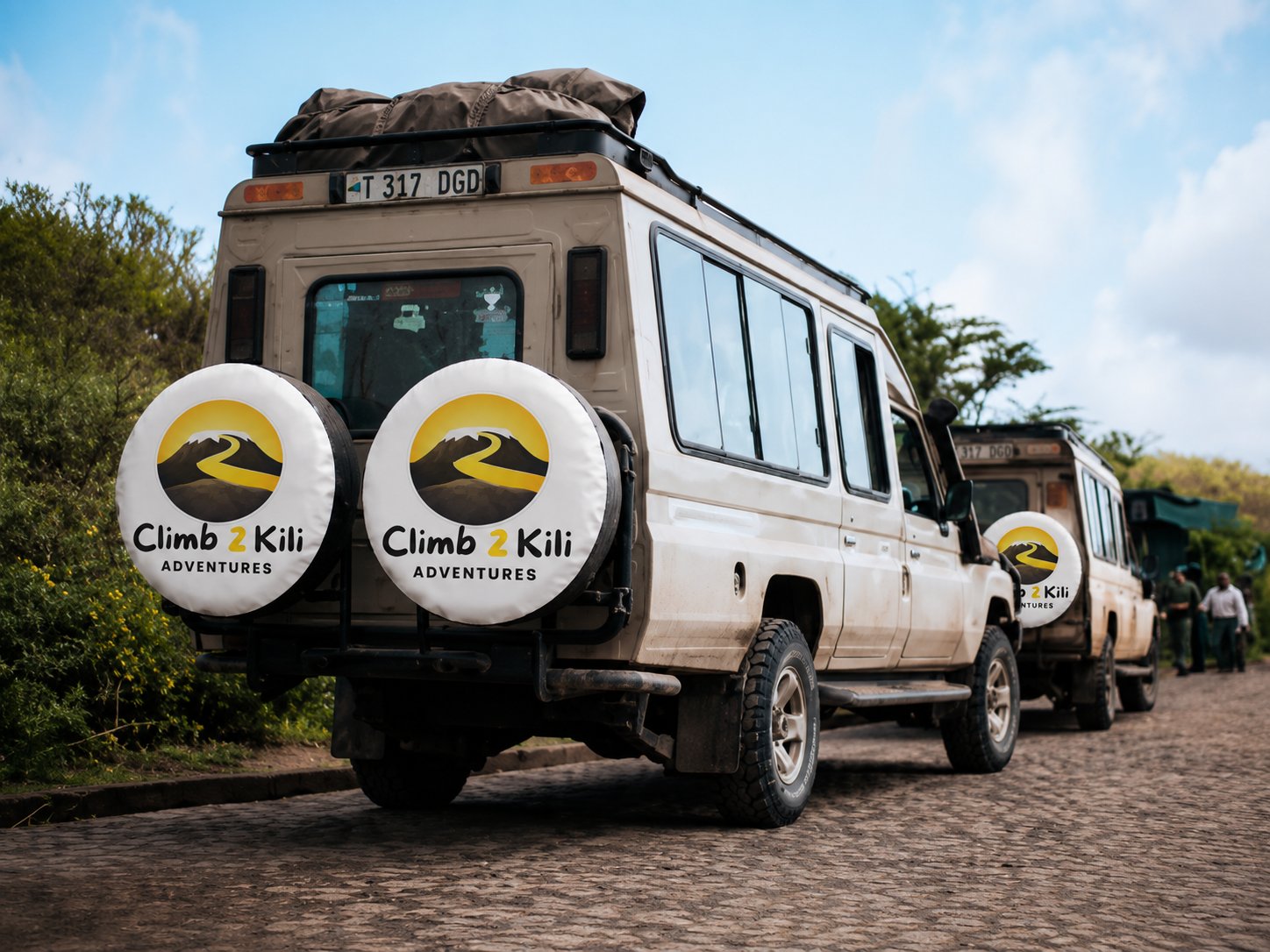 Founder standing with Kilimanjaro guides, porters, chefs, drivers, and local community members beneath Mount Kilimanjaro