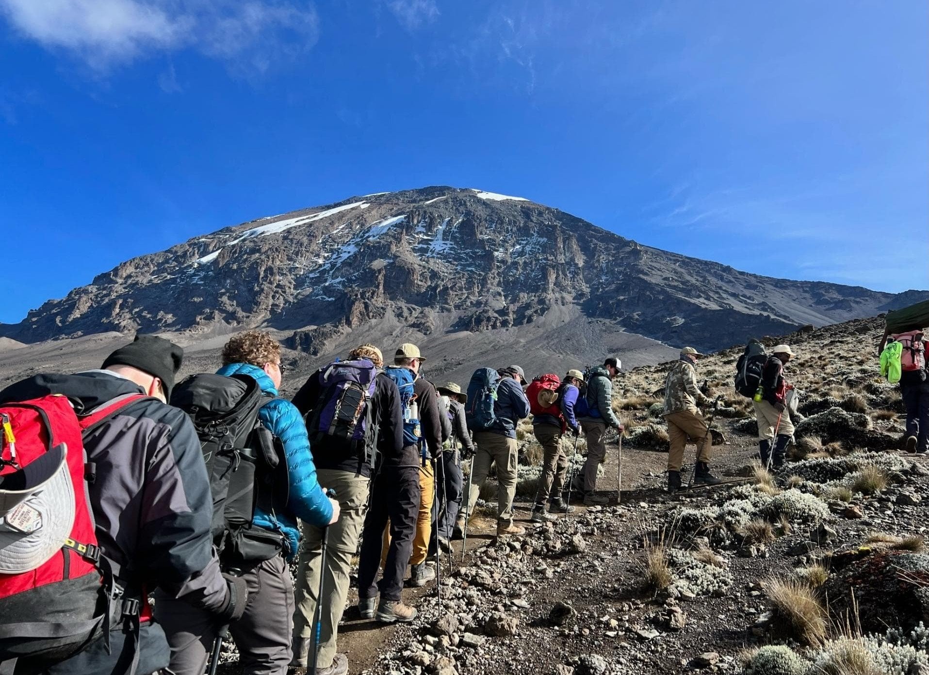 Beginner hikers trekking slowly through the Lemosho Route with mountain scenery and clouds