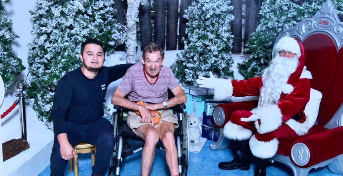 An everyday Ability Worker with a Client sitting next to Santa.