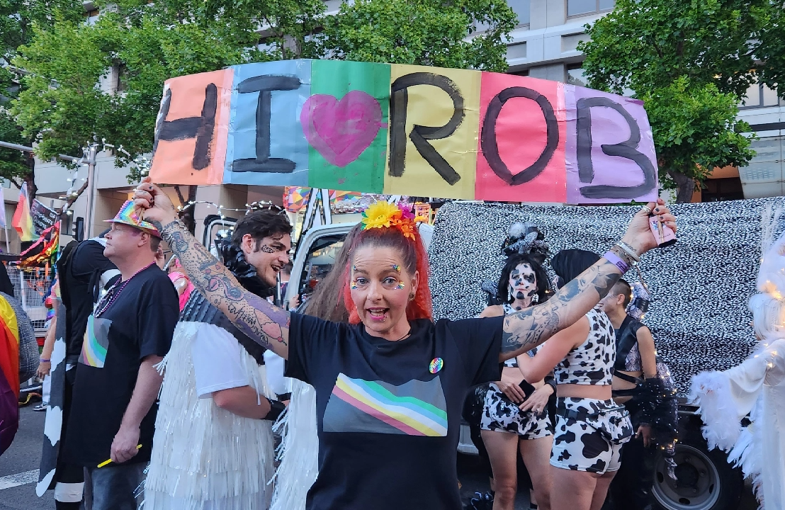 Woman holding a sign that says Hi Rob at a pride event