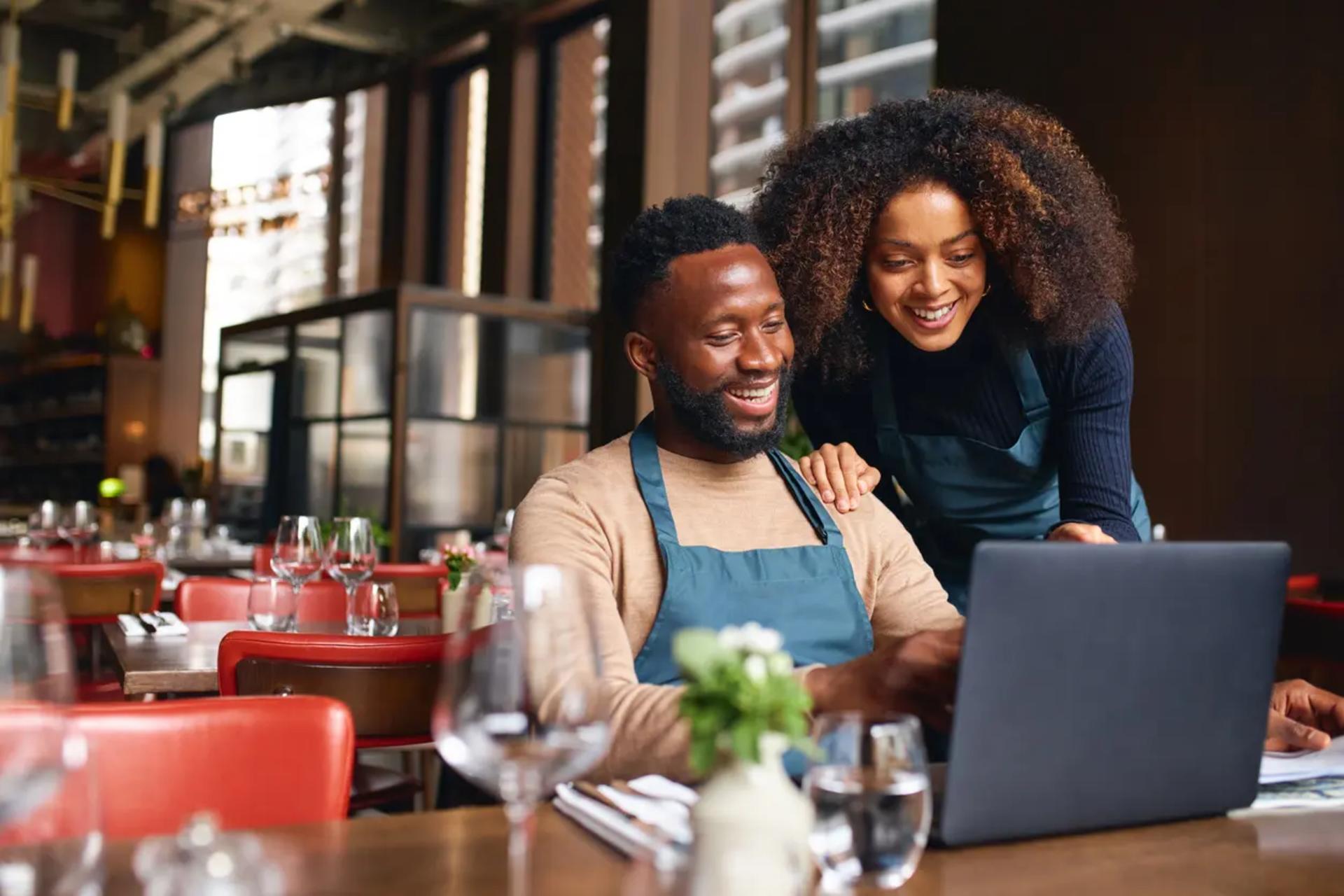 two small business owners using a laptop in their restaurant