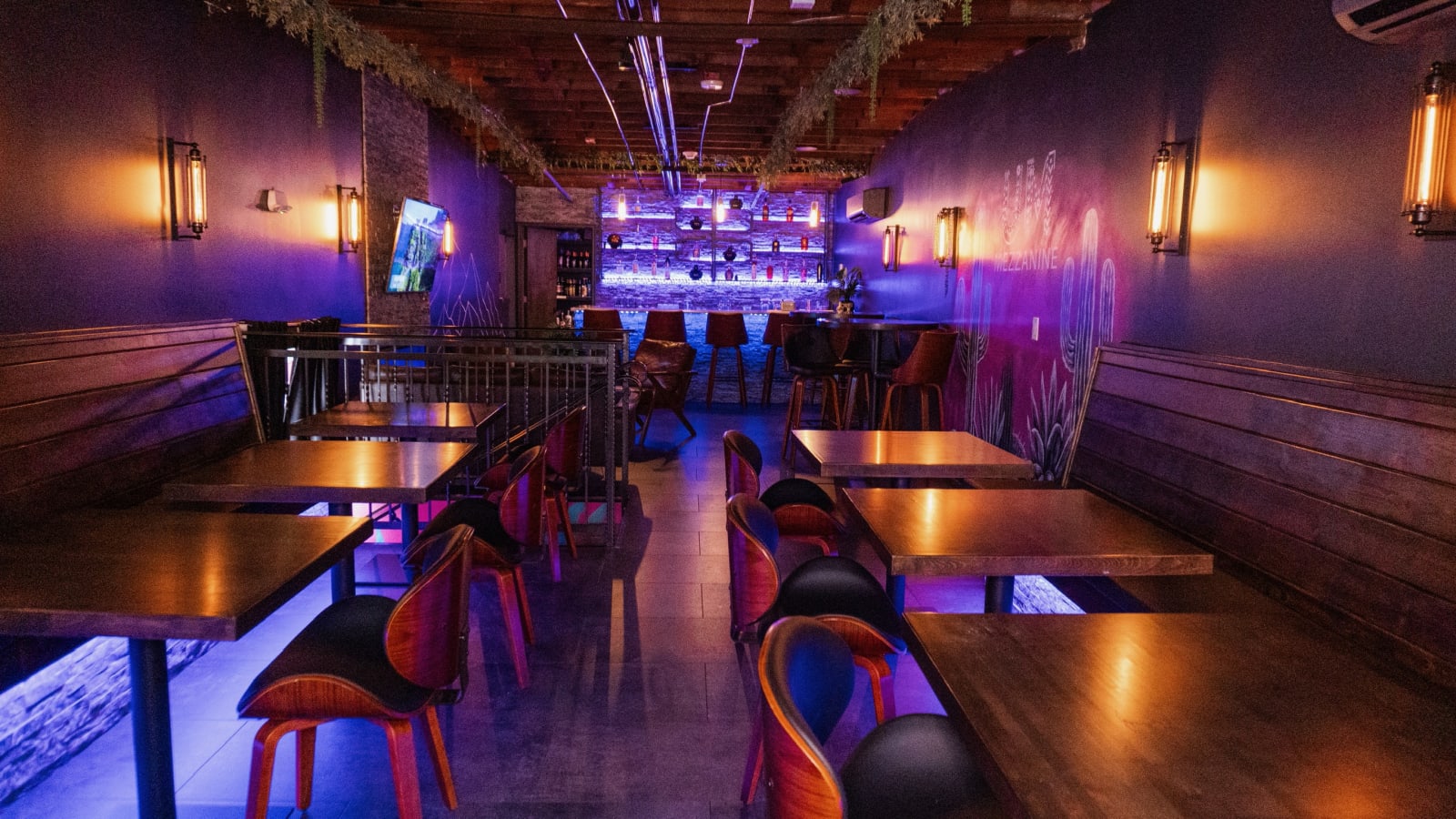 The Mezzanine at Uno Más — purple-lit upstairs lounge with the bar, booth seating, and agave mural
