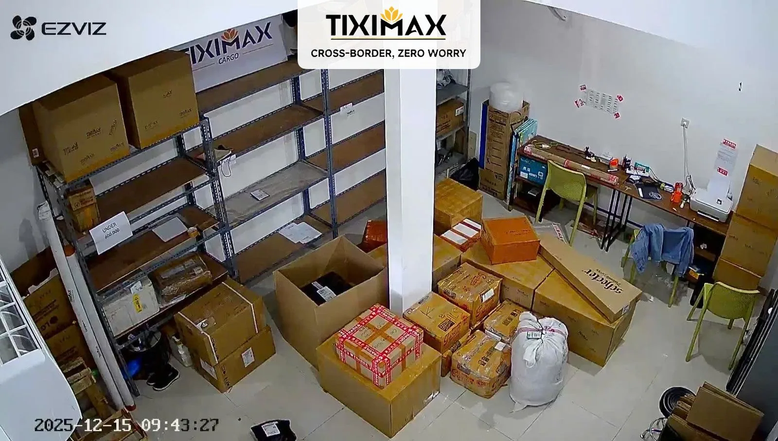 Kho hàng trống với kệ, thùng carton, bàn làm việc, camera an ninh.