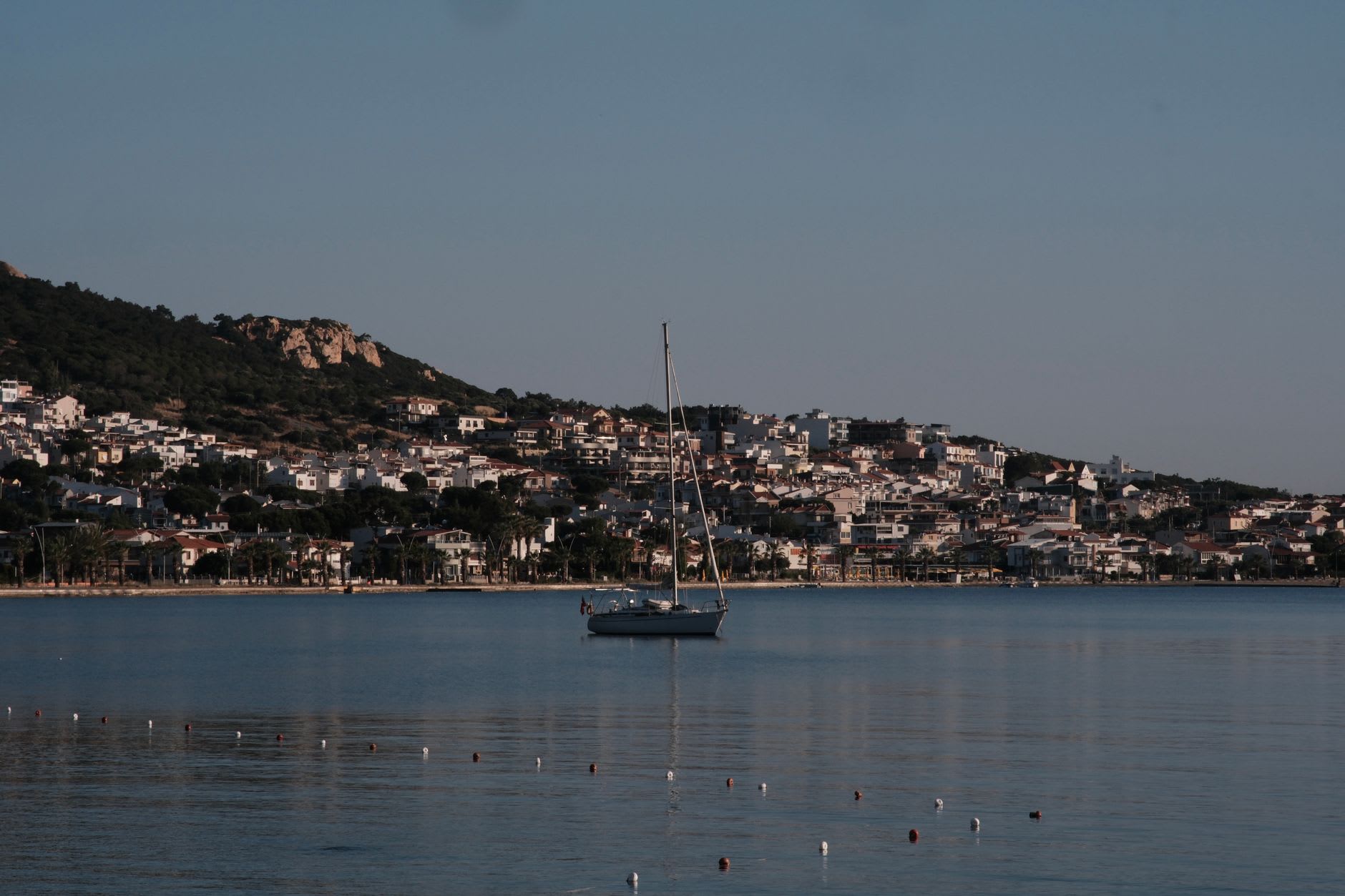Alaçatı's stone windmills on the ridge at sunset, wooden sails rotating slowly with the Aegean Sea visible in the distance
