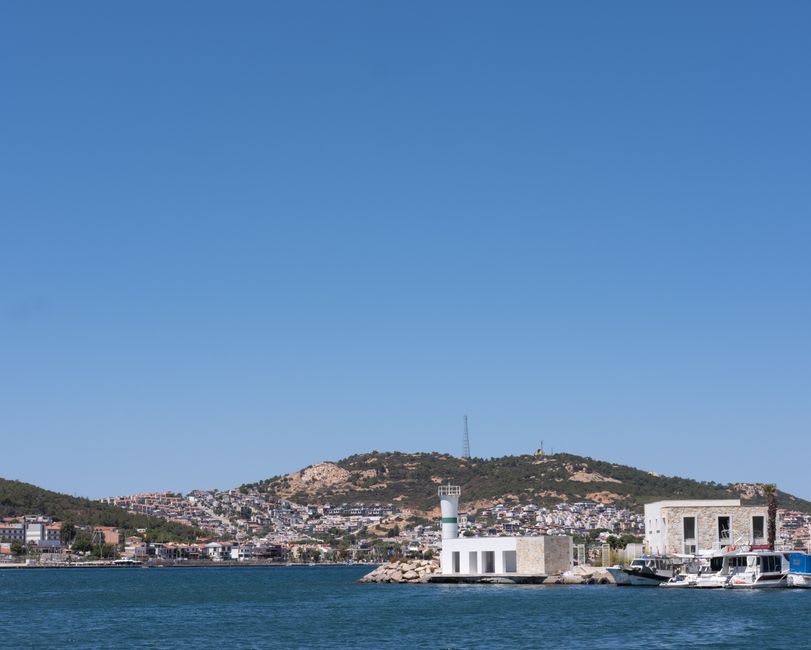 Un petit bateau de pêche en bois traversant la baie calme près de Foça avec deux îlots rocheux jumeaux visibles à l'arrière-plan