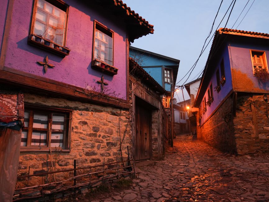 Narrow stone lane in Şirince lined with old Greek houses, overhanging balconies, and shuttered windows