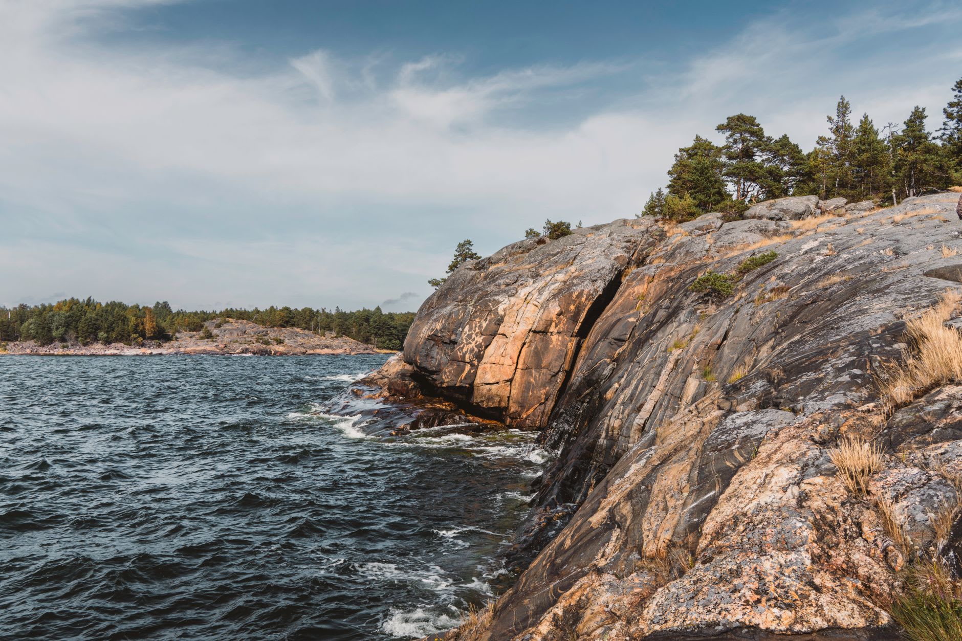 A chain of small granite islands in the Brändö municipality seen from the water at evening, reflections of orange sky and dark pines in calm channels between them