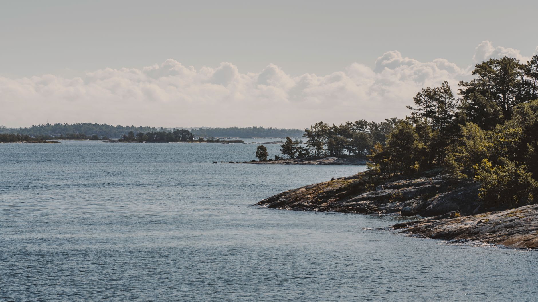 Wooden dock and village of Lappo in Brändö at sunset, with traditional painted houses, a few fishing boats, and the outer islands silhouetted in the distance