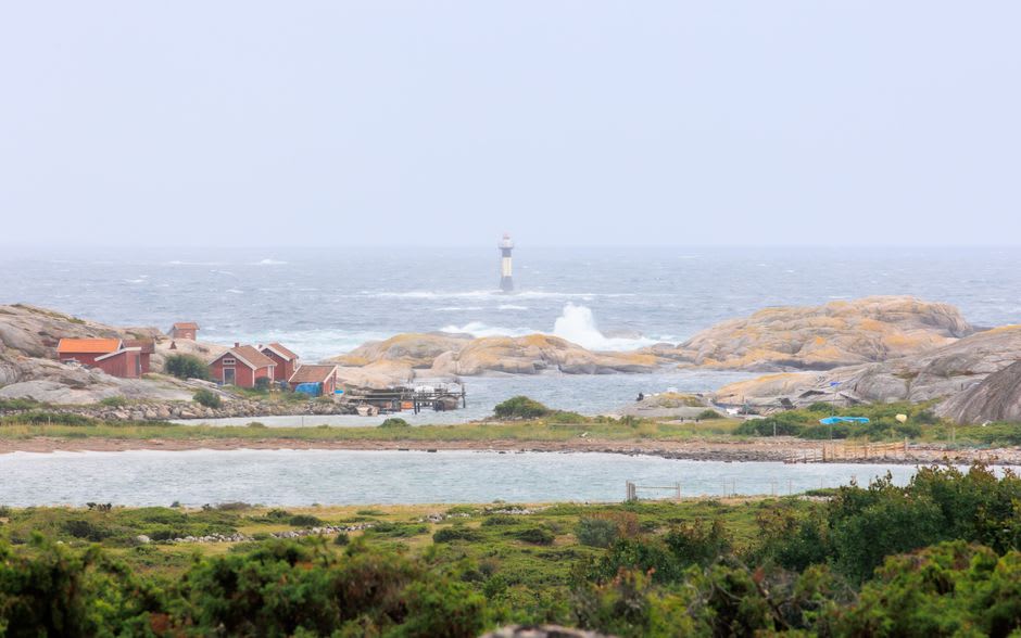 Weathered red wooden pilot cottages on the bare granite of Kobba Klintar skerry with a small white lighthouse behind them