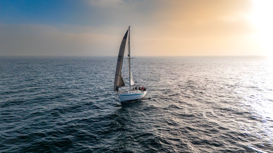 Calm water of Lumparn bay at sunset with a small sailing dinghy and low forested shoreline of Lumparland in the distance