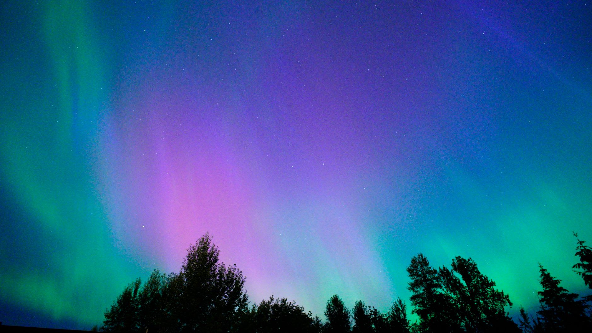 Northern lights aurora in multiple colors reflected in a partially frozen lake outside Fairbanks