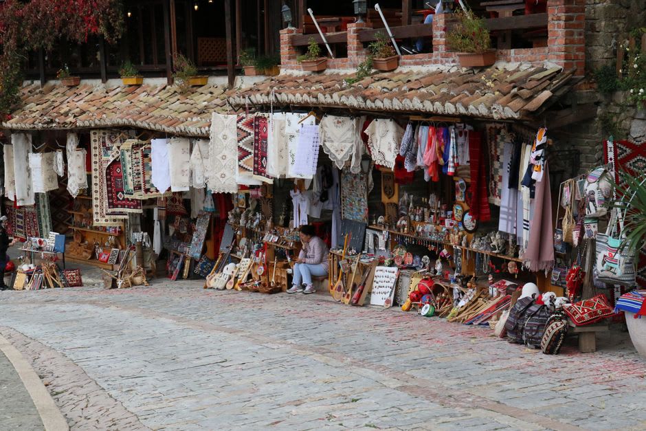 Wooden stalls in the Old Bazaar of Krujë displaying hammered copper pots and woven rugs