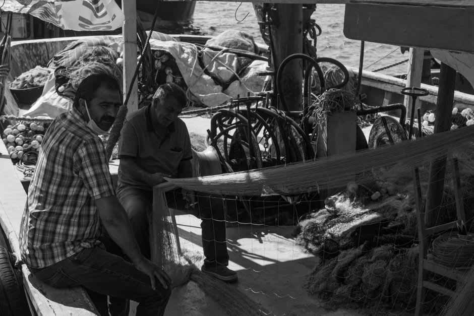 Pescadores preparando redes junto a pequeñas barcas de madera en el puerto de Pogradec a primera hora de la mañana