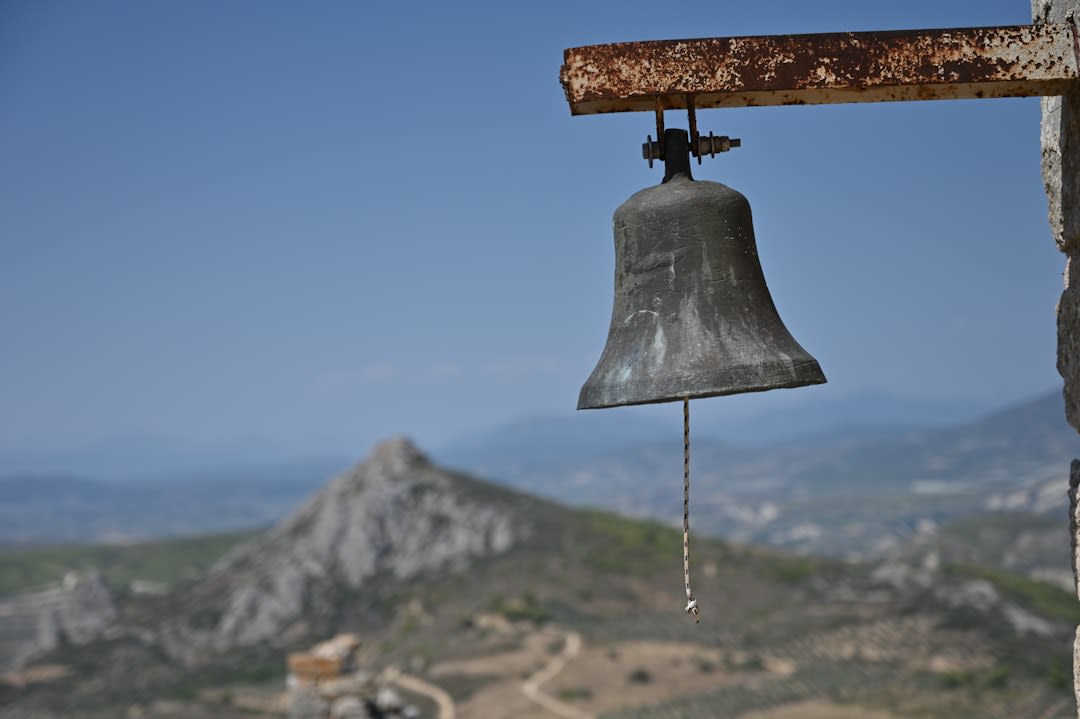 A weathered stone church with a bell tower standing in a grassy clearing in Voskopojë