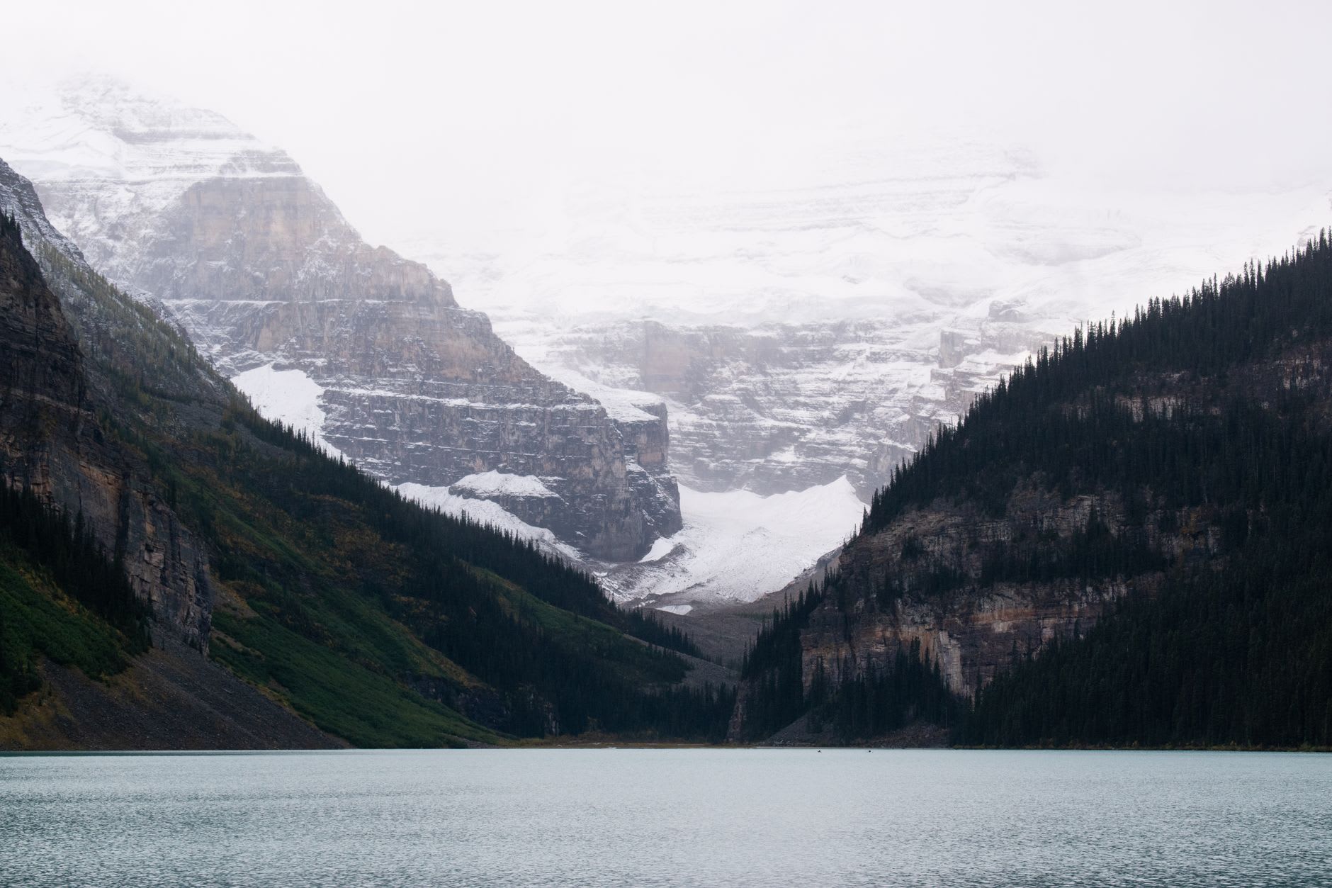 La face inférieure du glacier Victoria se reflétant dans l'eau plate du lac Louise à la première lumière, sans vent, une fine brume à l'extrémité lointaine