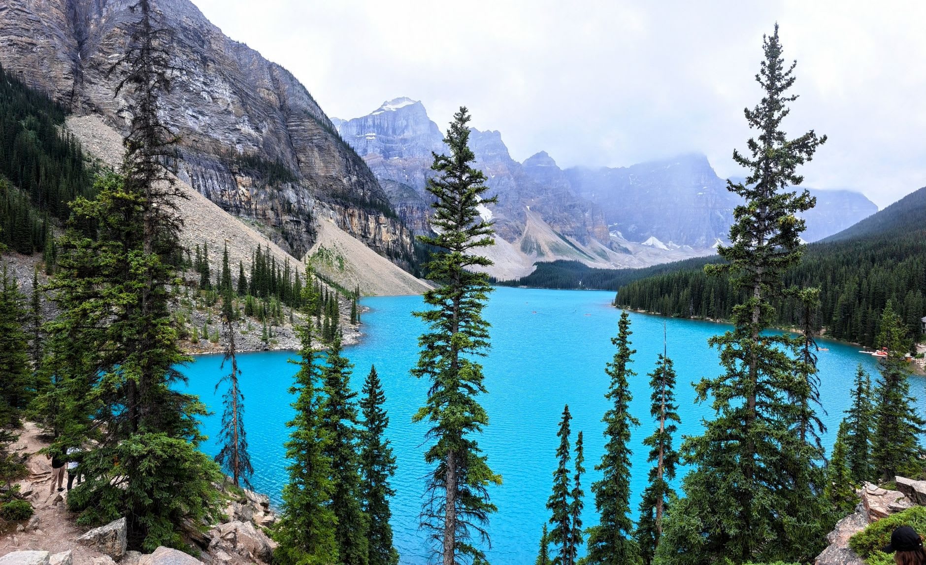 The Rockpile viewpoint at Moraine Lake with a handful of people silhouetted against the early morning light, ten peaks lit in sequence behind them