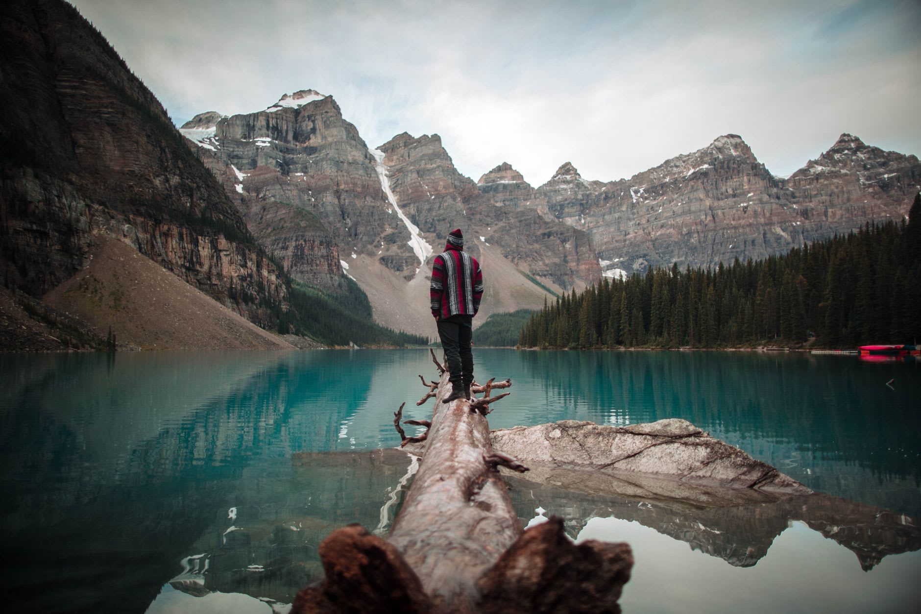 A red canoe on Moraine Lake, paddler making their way toward the far shore, the ten peaks reflected in the water beside them