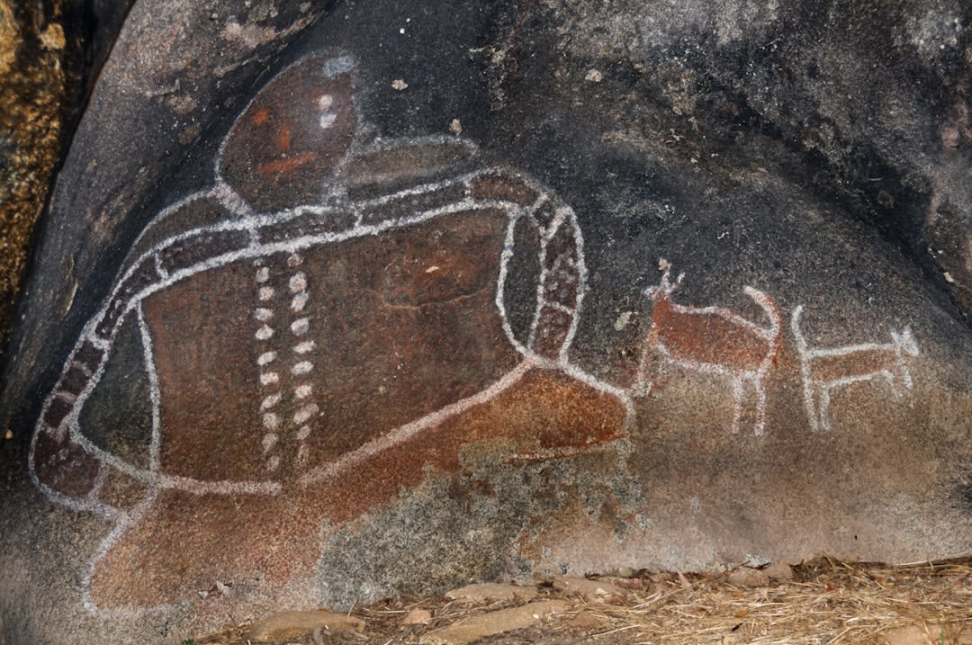 Ancient petroglyphs of shield-bearing warriors carved into a sandstone rock face at Writing-on-Stone, weathered but still legible after centuries