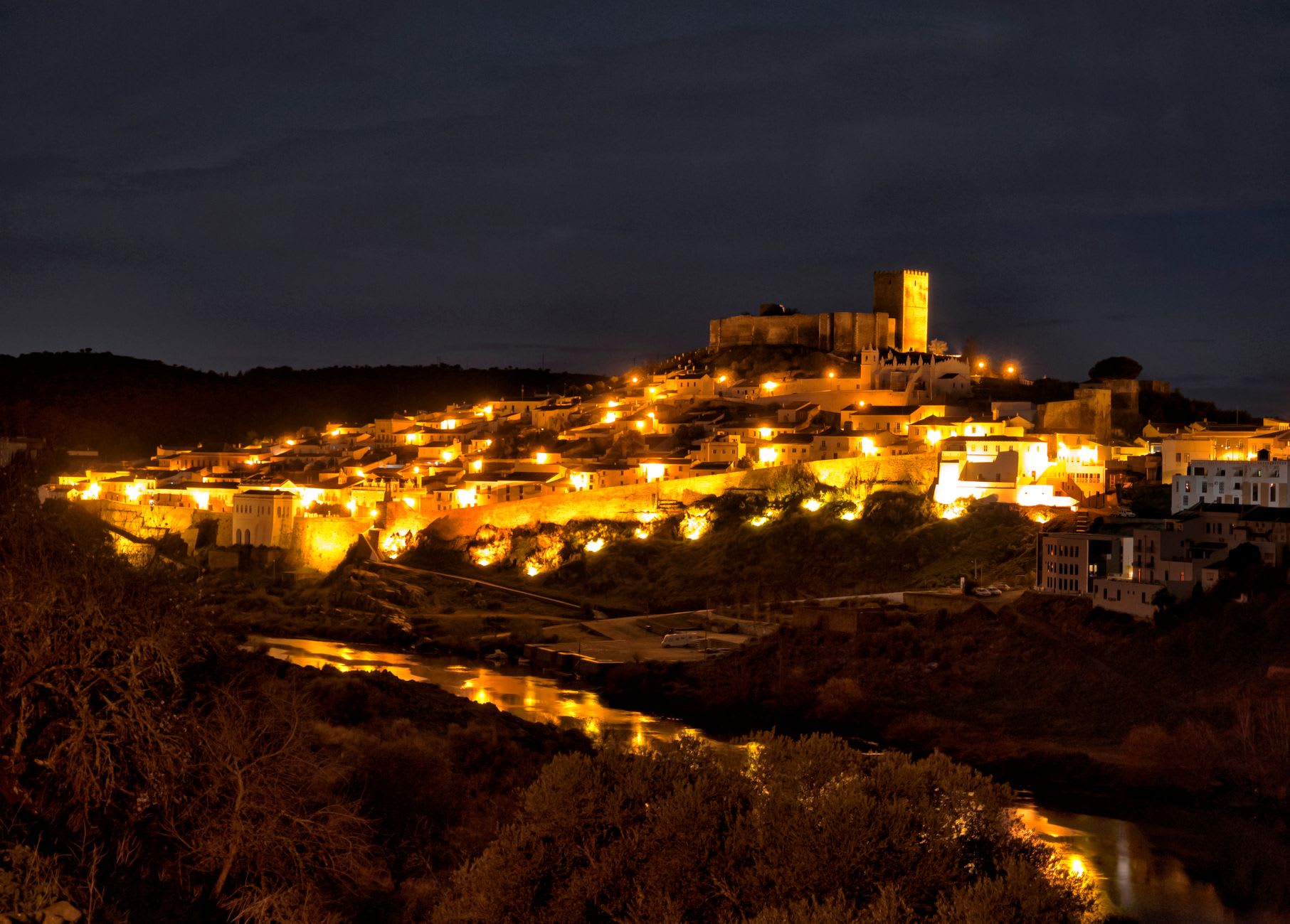 La Torre de Menagem de Beja vista desde la calle de abajo, sus muros de piedra elevándose dramáticamente contra un cielo azul caluroso