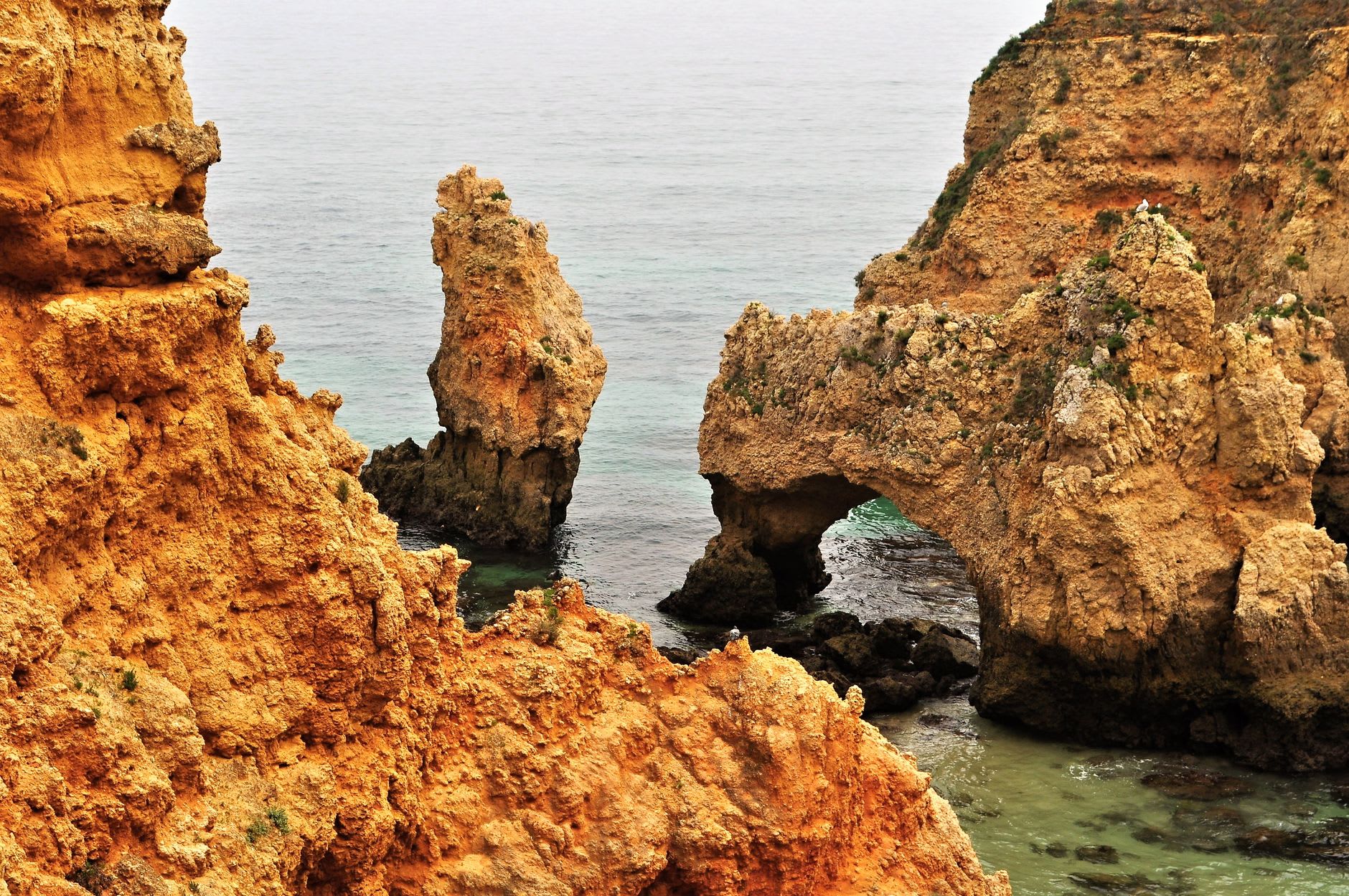 Two kayakers paddling through a narrow sea arch at Ponta da Piedade with golden rock walls towering on both sides