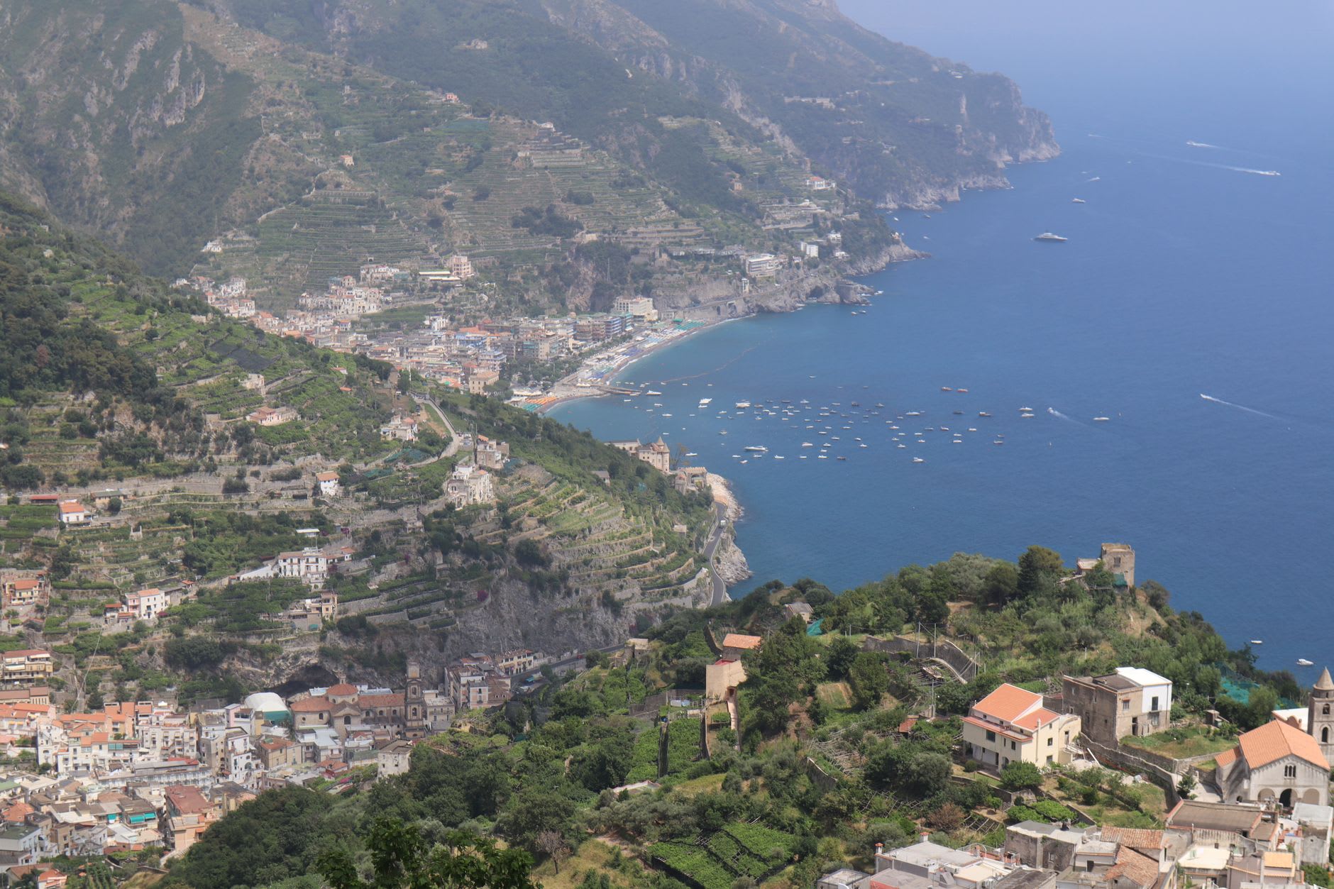 The Sentiero degli Dei ridge trail in May, with wildflowers along the path edge and Positano visible far below on the left
