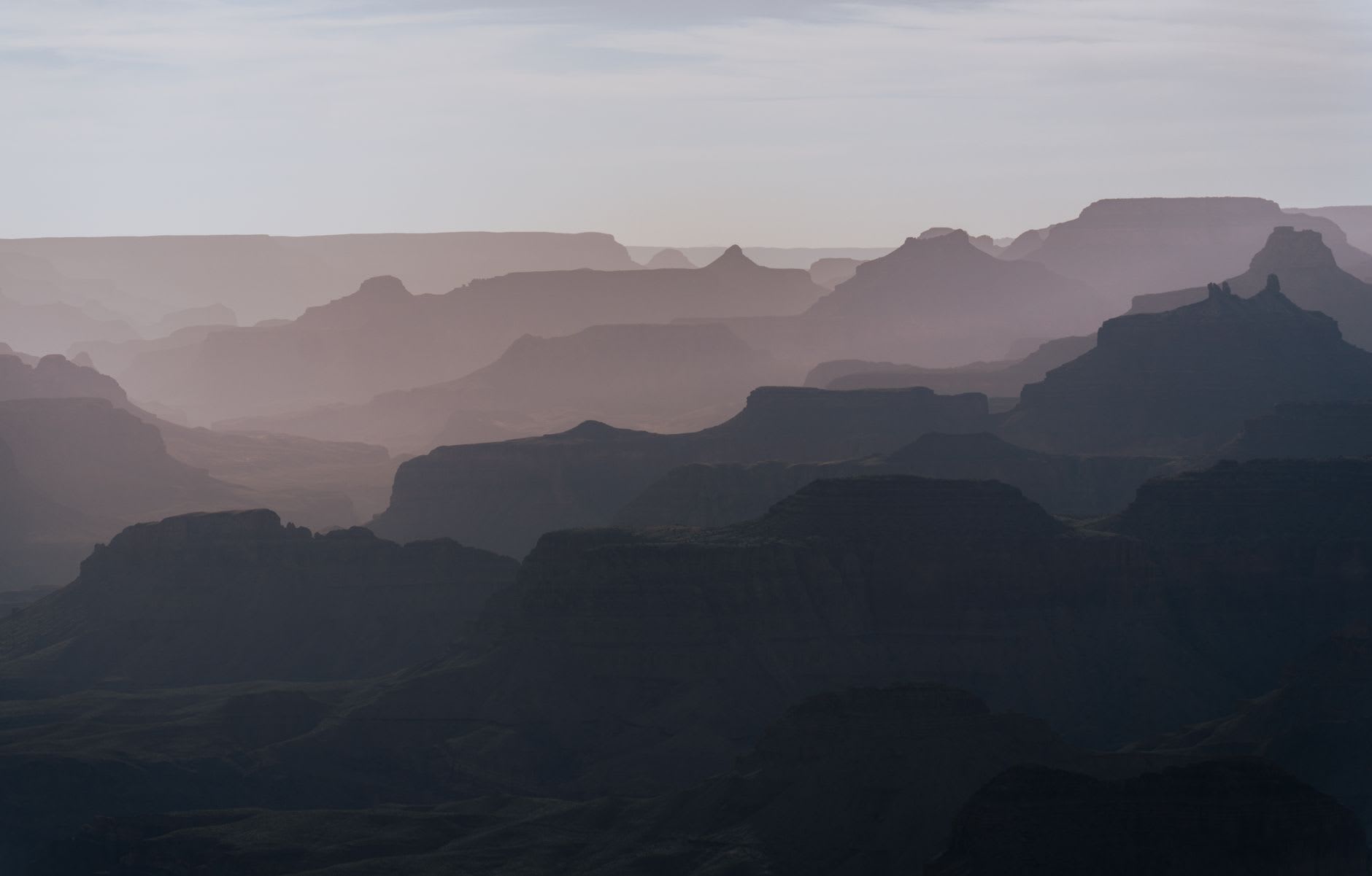 The first light of sunrise catching the canyon walls in shades of amber and rose while the inner gorge remains in shadow