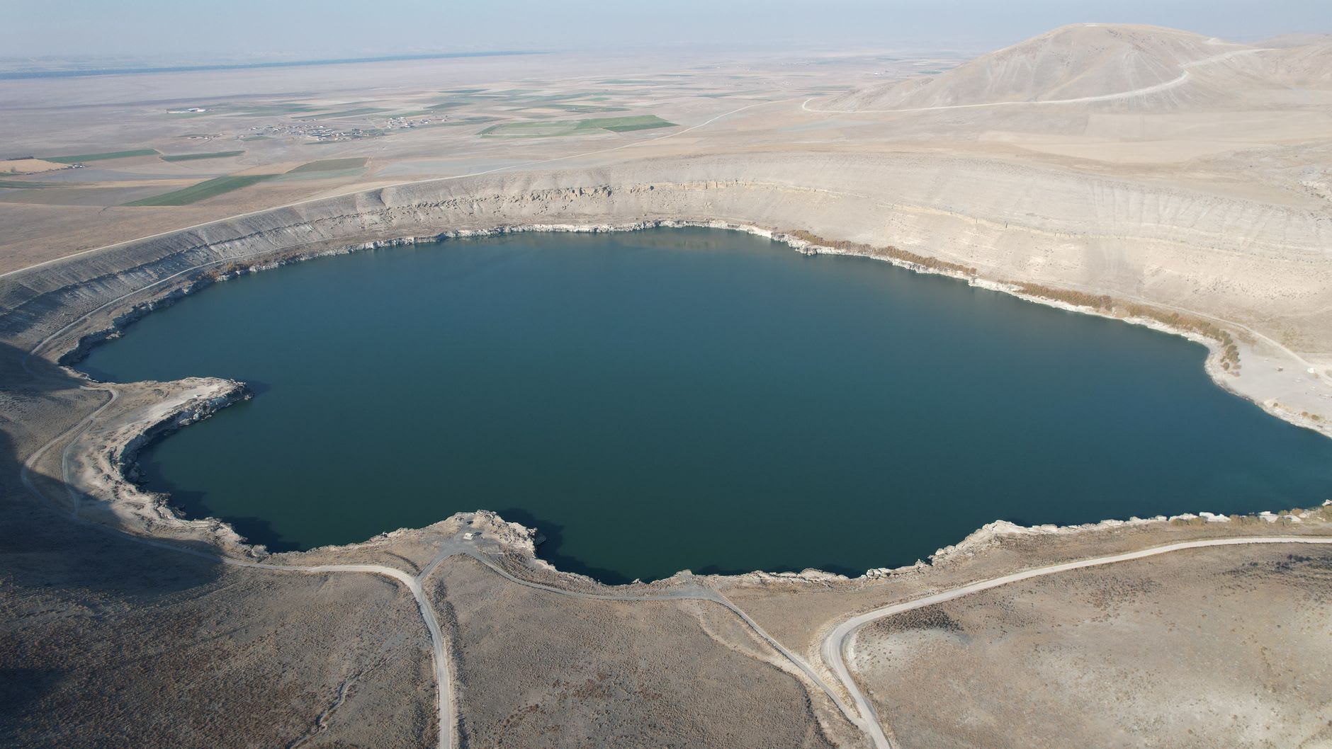 The conical island at the centre of Meke Crater Lake, reflected in the shallow salt-tinged water of the maar, under a wide Anatolian sky