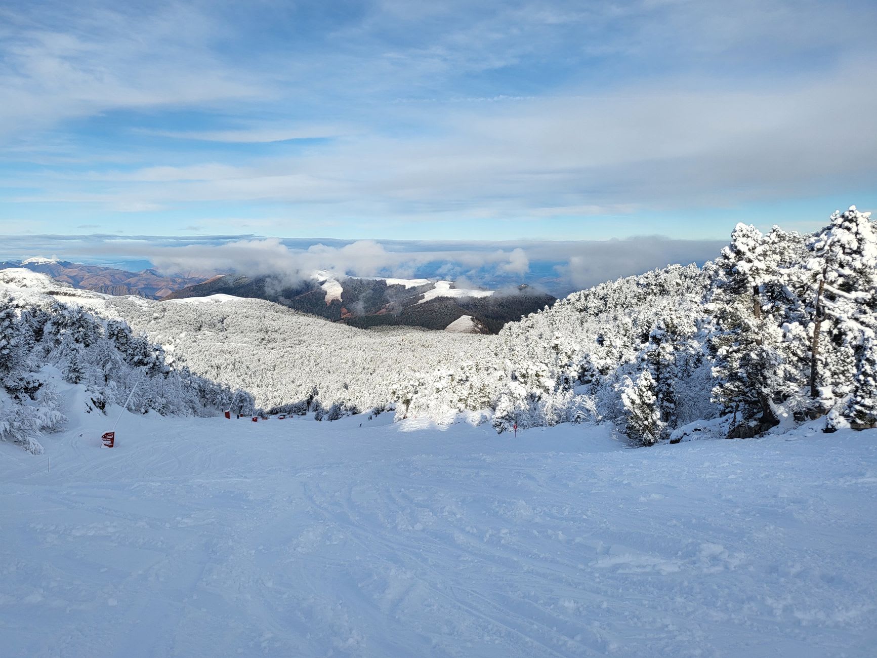 Skiers on a wide red piste at Grandvalira with the Andorran valley visible far below through cold mountain air