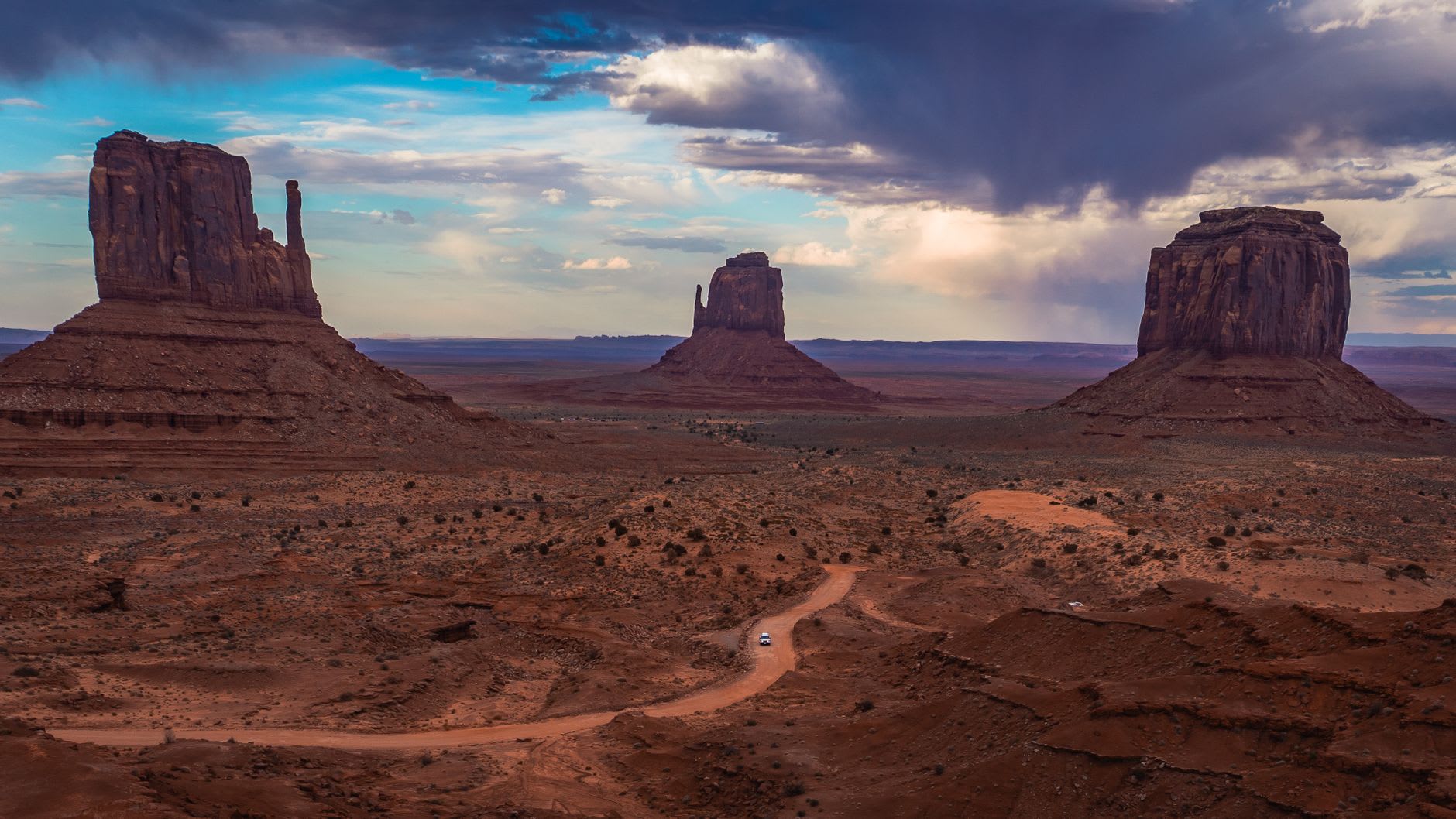 La formación de las Tres Hermanas captando la última luz naranja del atardecer en Monument Valley, el cielo tornándose púrpura intenso detrás