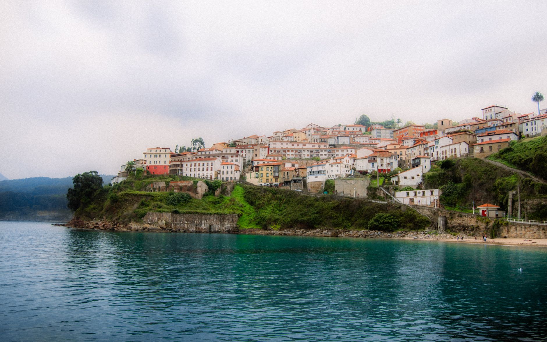 Cudillero's harbor from above, with fishing boats on the water and the village's painted houses cascading down the hillside