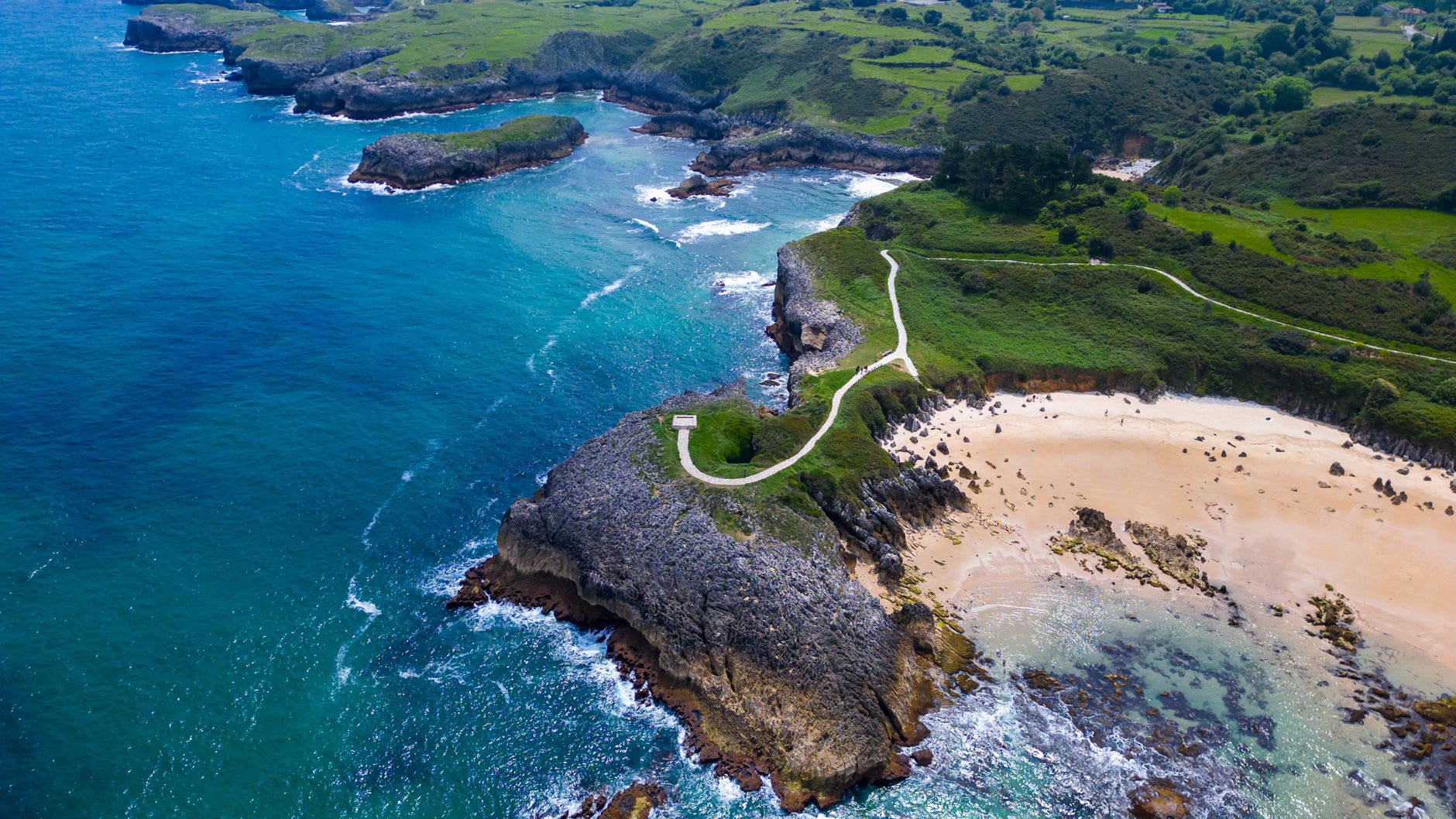 A hidden beach east of Llanes — white sand crescent enclosed by limestone cliffs with impossibly clear water