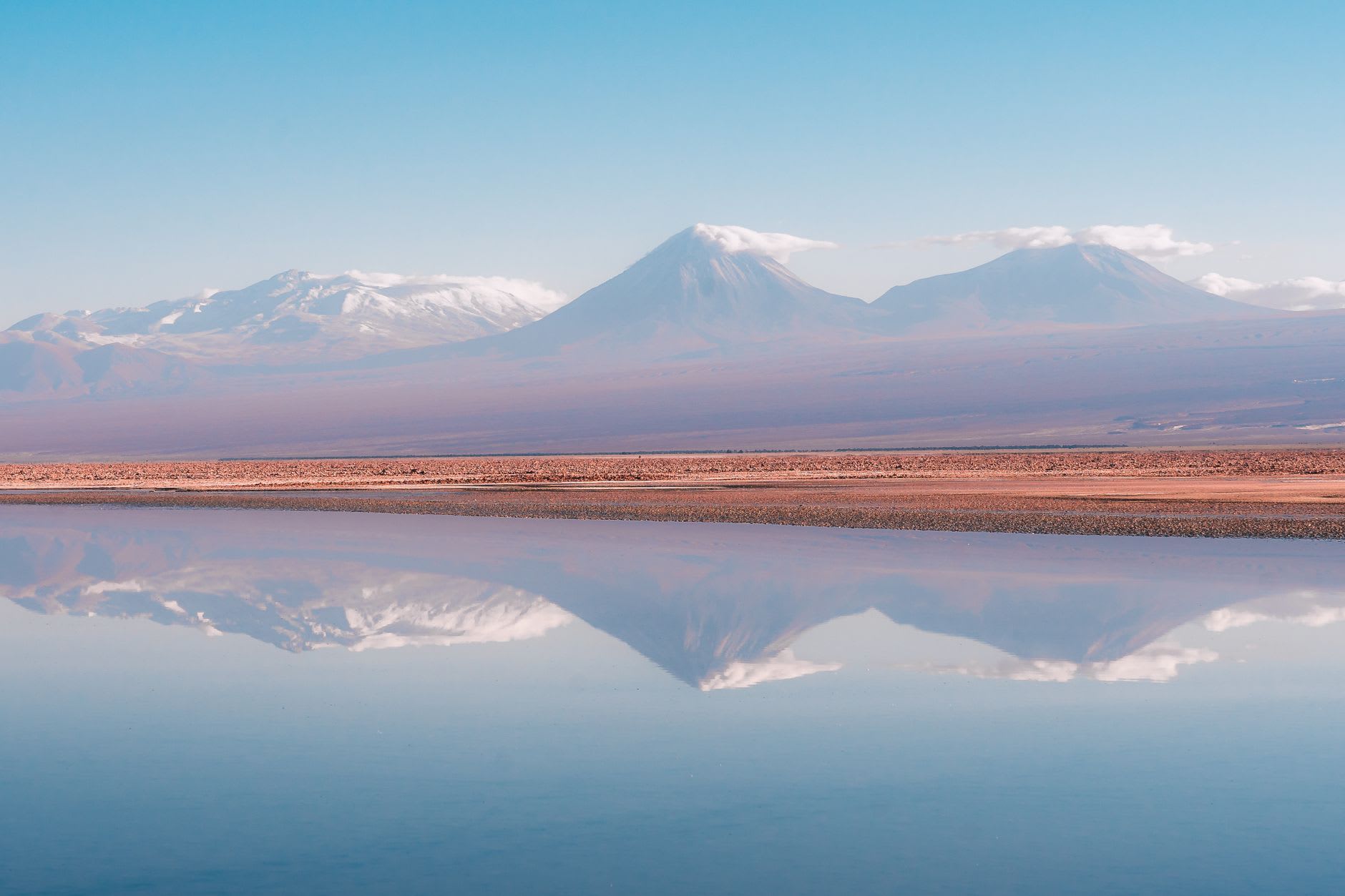 Iron-red rocks scattered along the shore of a vivid turquoise altiplano lagoon under a deep blue sky