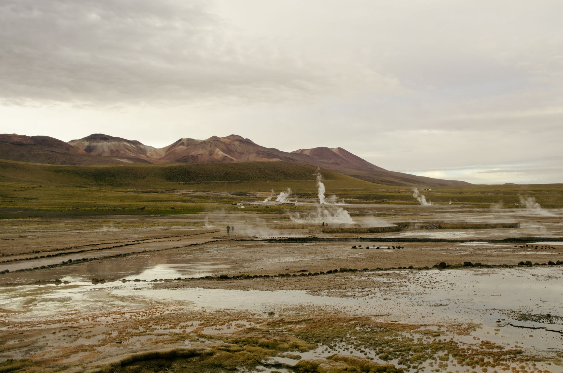 Les bassins inférieurs à Puritama avec les parois du canyon reflétées dans l'eau chaude et immobile sous un ciel bleu sans nuages