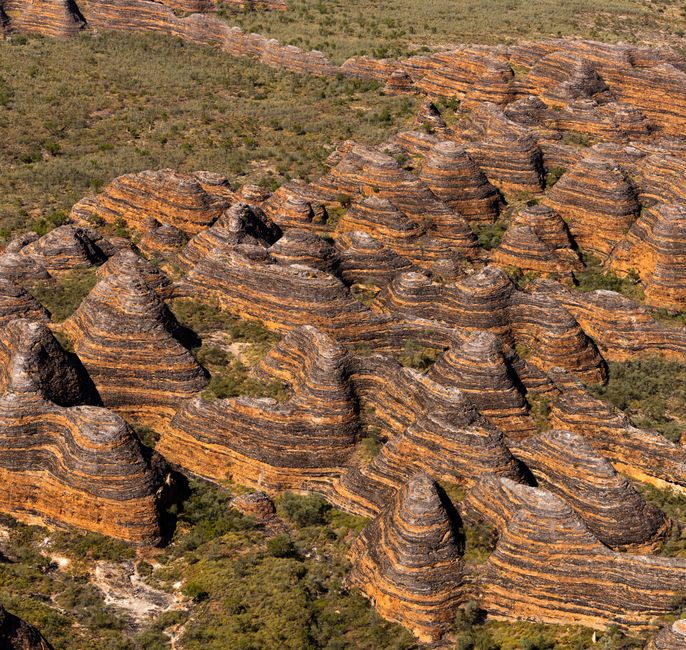 Vista aérea de las cúpulas rayadas del Bungle Bungle Range elevándose desde la meseta del Kimberley, con bandas naranja y negras sobre la tierra roja ancestral