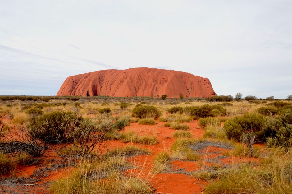 Uluru emergiendo del paisaje rojo del interior australiano bajo un amplio cielo desértico