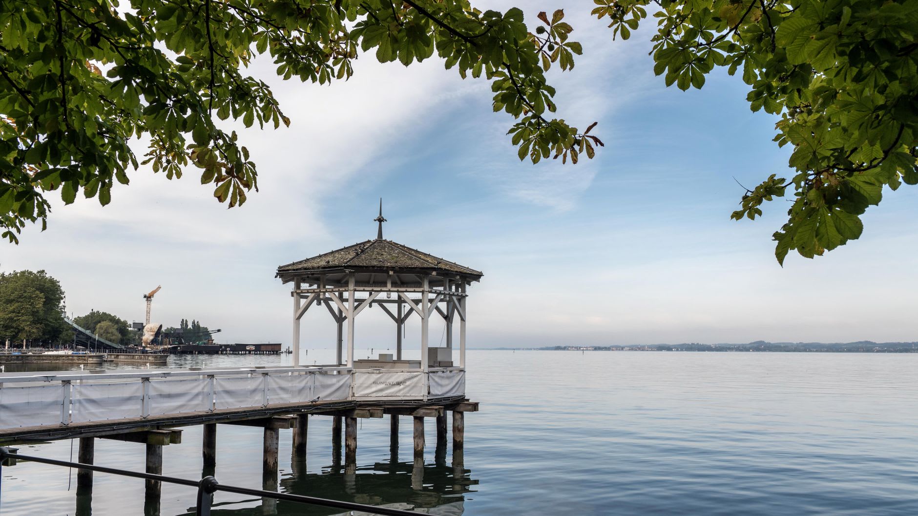 The Wörthersee shoreline at Strandbad Klagenfurt, wooden piers stretching into the warm green-blue water on a clear summer morning